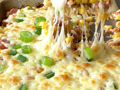 A sheet pan filled with creamy golden corn, sliced smoked sausage, and melted mozzarella cheese.