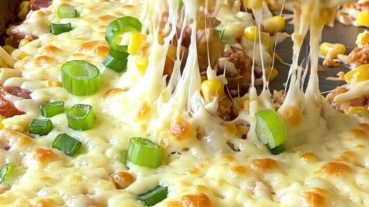 A sheet pan filled with creamy golden corn, sliced smoked sausage, and melted mozzarella cheese.