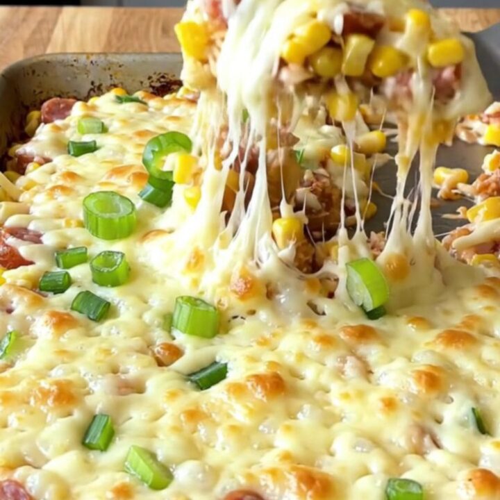 A sheet pan filled with creamy golden corn, sliced smoked sausage, and melted mozzarella cheese.