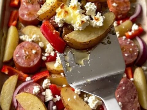 A vibrant sheet pan filled with golden potato wedges, browned kielbasa, soft red peppers, and crumbled feta cheese.