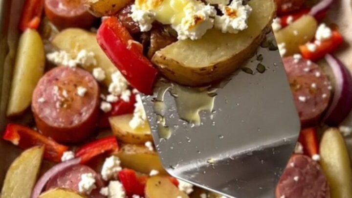 A vibrant sheet pan filled with golden potato wedges, browned kielbasa, soft red peppers, and crumbled feta cheese.