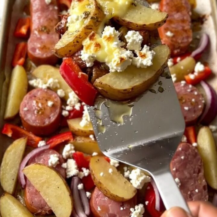 A vibrant sheet pan filled with golden potato wedges, browned kielbasa, soft red peppers, and crumbled feta cheese.