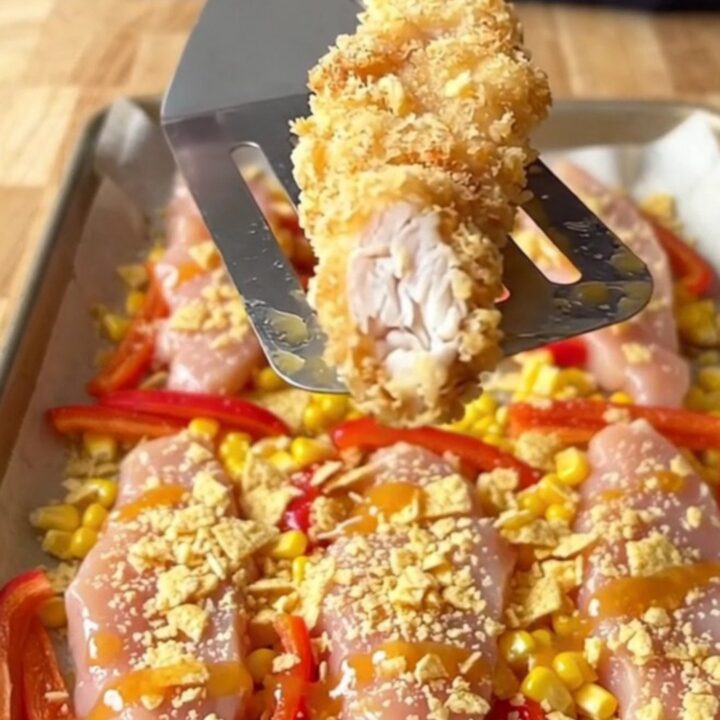 A sheet pan filled with golden, crispy tortilla-crusted chicken tenders, roasted corn, and red pepper strips.