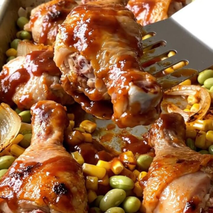 A sheet pan filled with golden-brown chicken drumsticks, roasted corn kernels, butter beans