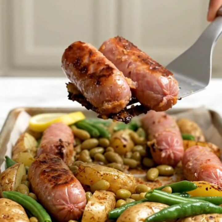 Parchment-lined sheet pan filled with roasted Italian sausages, golden baby potatoes, green beans, and lemon slices.