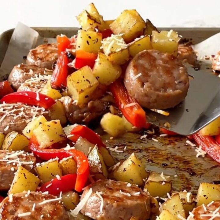 A sheet pan filled with golden roasted potatoes, sliced chicken sausage, and colorful bell peppers.