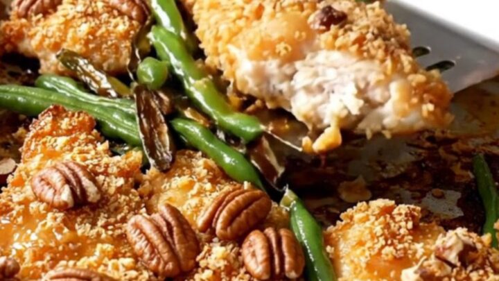 A sheet pan filled with golden pecan-crusted chicken tenders and roasted green beans on a white countertop.