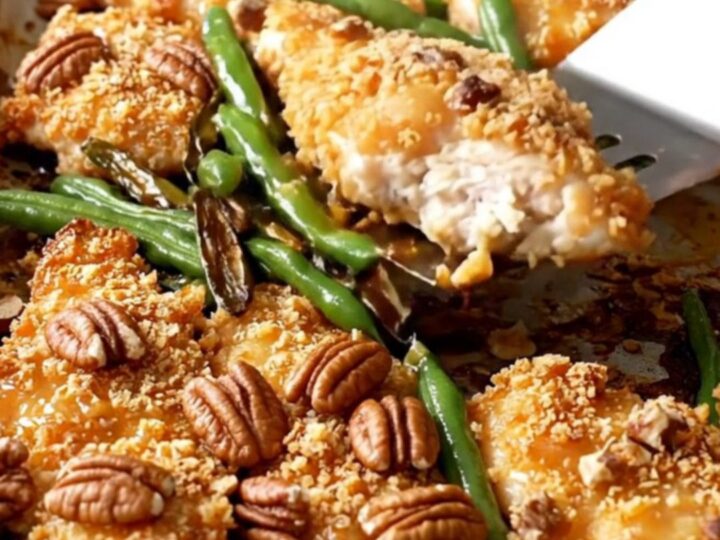 A sheet pan filled with golden pecan-crusted chicken tenders and roasted green beans on a white countertop.