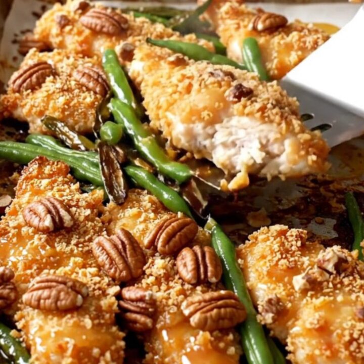 A sheet pan filled with golden pecan-crusted chicken tenders and roasted green beans on a white countertop.