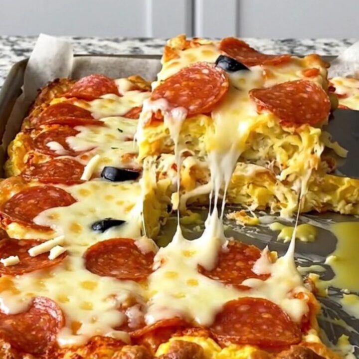 A top-down view of a sheet pan filled with golden-baked pepperoni pizza eggs on a speckled granite countertop.
