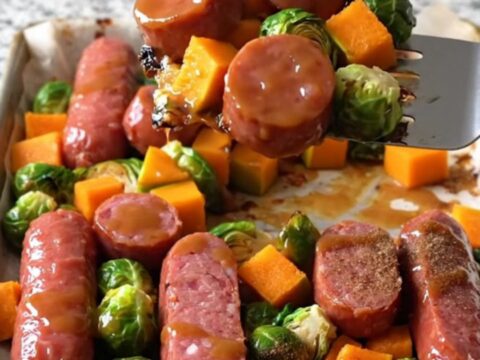 A sheet pan filled with golden-brown kielbasa coins, roasted butternut squash, and crispy Brussels sprouts glazed with maple.