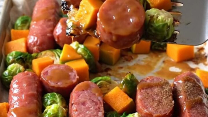 A sheet pan filled with golden-brown kielbasa coins, roasted butternut squash, and crispy Brussels sprouts glazed with maple.