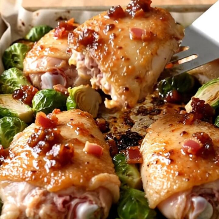 A sheet pan filled with golden-brown roasted chicken thighs and caramelized Brussels sprouts topped with bacon jam.