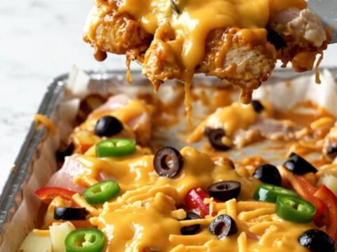 A sheet pan filled with golden roasted chicken chunks, crispy potatoes, and melted cheddar topped with jalapenos and olives.