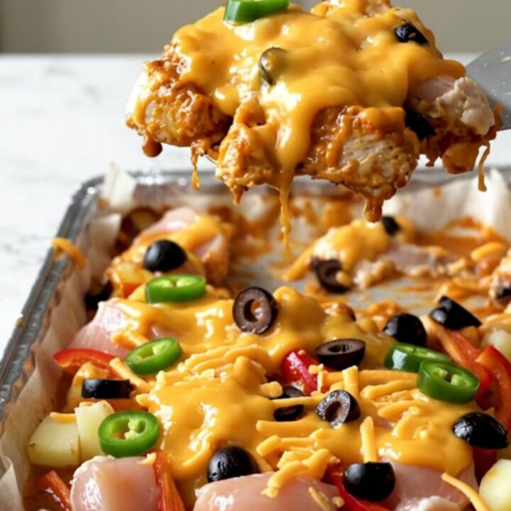 A sheet pan filled with golden roasted chicken chunks, crispy potatoes, and melted cheddar topped with jalapenos and olives.