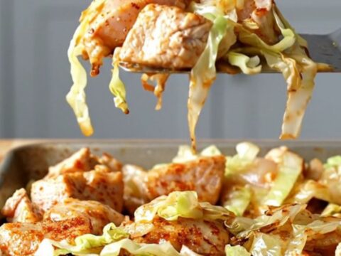 A sheet pan filled with golden-brown roasted chicken, tender cabbage, onions, and bell peppers.