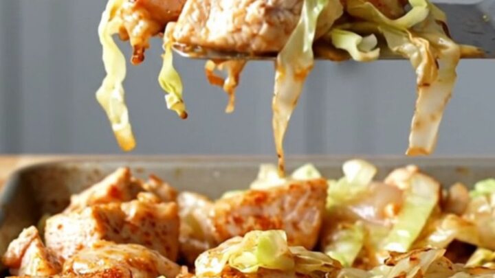 A sheet pan filled with golden-brown roasted chicken, tender cabbage, onions, and bell peppers.