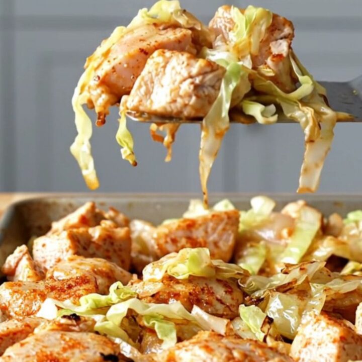A sheet pan filled with golden-brown roasted chicken, tender cabbage, onions, and bell peppers.