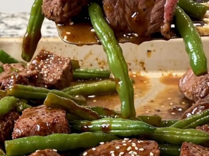 A sheet pan filled with golden-brown beef cubes, blistered green beans, and charred onion wedges, finished with sesame seeds.