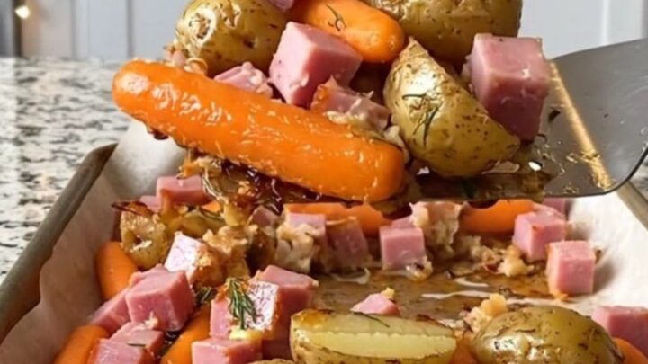 A sheet pan filled with golden roasted potatoes, orange carrots, and savory ham cubes, garnished with fresh dill.