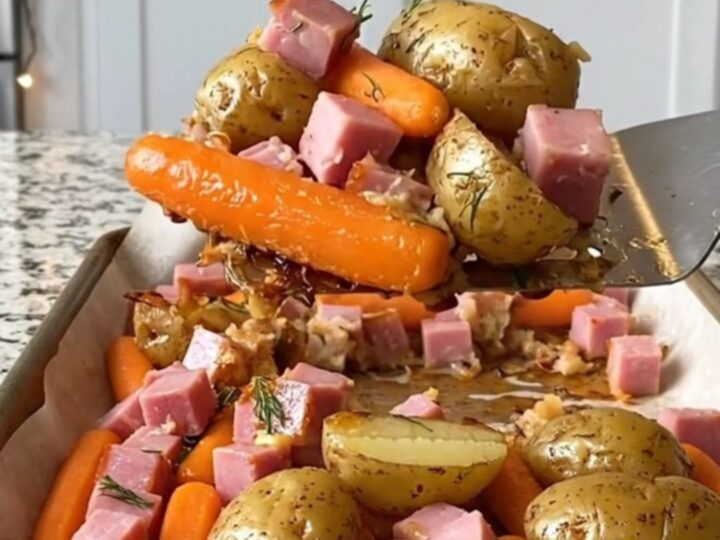 A sheet pan filled with golden roasted potatoes, orange carrots, and savory ham cubes, garnished with fresh dill.
