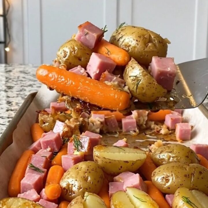 A sheet pan filled with golden roasted potatoes, orange carrots, and savory ham cubes, garnished with fresh dill.