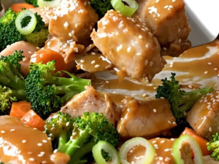 A sheet pan filled with golden-tan roasted chicken chunks, bright green broccoli florets, and orange carrot coins.