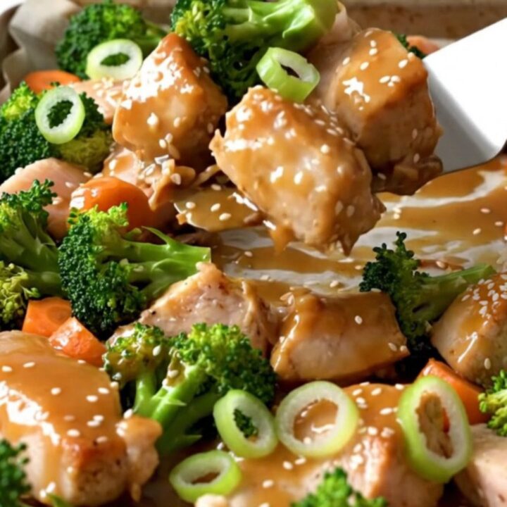 A sheet pan filled with golden-tan roasted chicken chunks, bright green broccoli florets, and orange carrot coins.