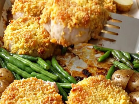 A sheet pan filled with golden-crusted pork tenderloin rounds, roasted baby potatoes, and bright green beans.