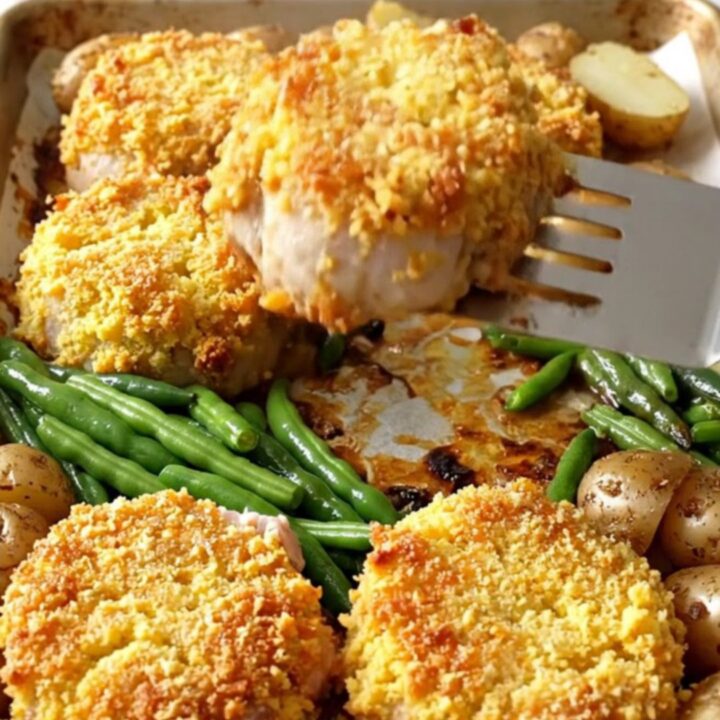 A sheet pan filled with golden-crusted pork tenderloin rounds, roasted baby potatoes, and bright green beans.