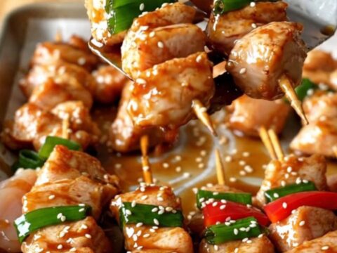 A sheet pan filled with golden-brown chicken chunks, vibrant red peppers, and charred green onions.