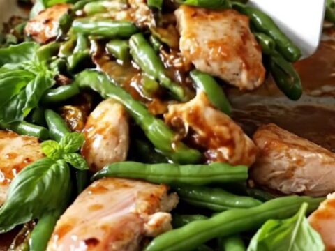 A sheet pan filled with golden-tan chicken breast chunks, blistered green beans, and red pepper strips