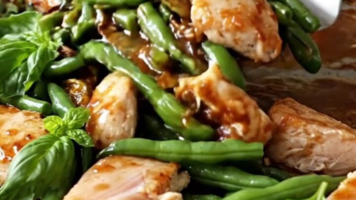 A sheet pan filled with golden-tan chicken breast chunks, blistered green beans, and red pepper strips