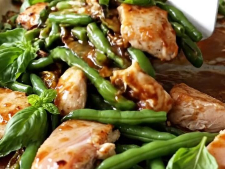A sheet pan filled with golden-tan chicken breast chunks, blistered green beans, and red pepper strips