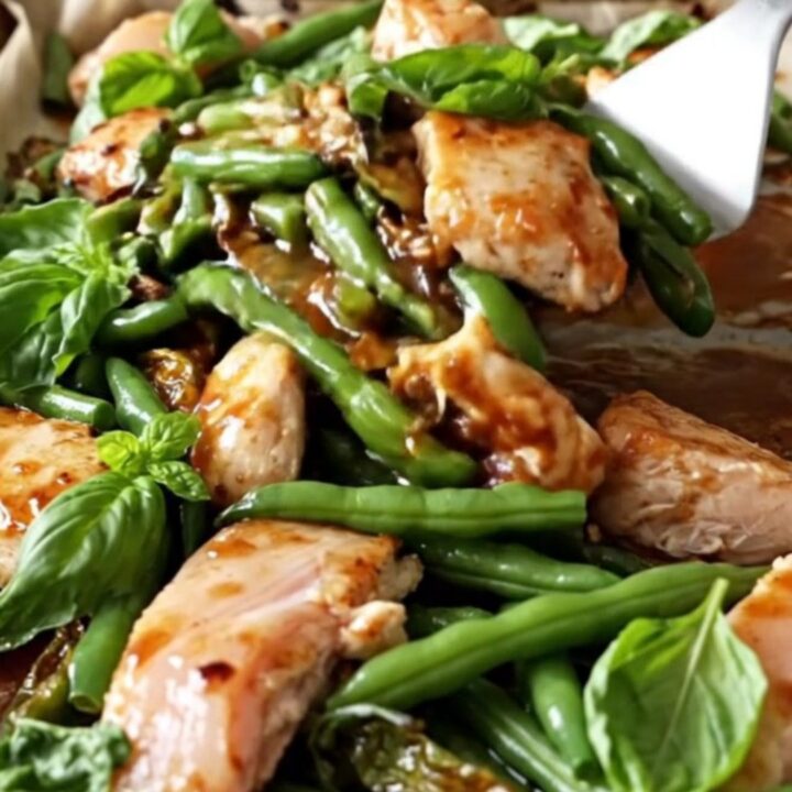 A sheet pan filled with golden-tan chicken breast chunks, blistered green beans, and red pepper strips