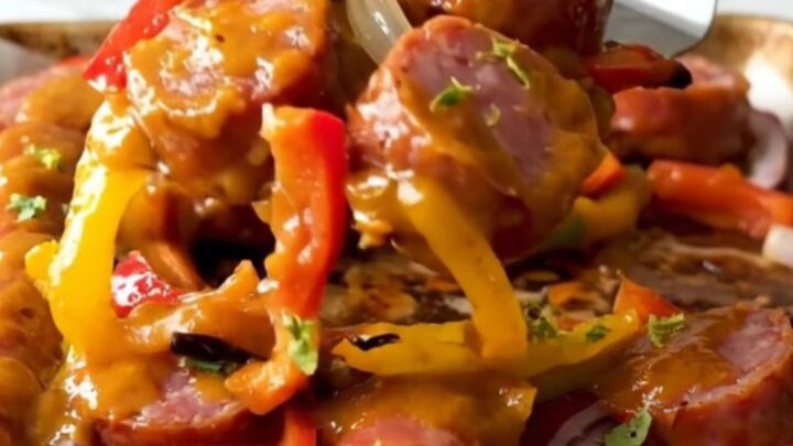 A sheet pan filled with golden-brown kielbasa coins, vibrant bell pepper chunks, and red onion wedges