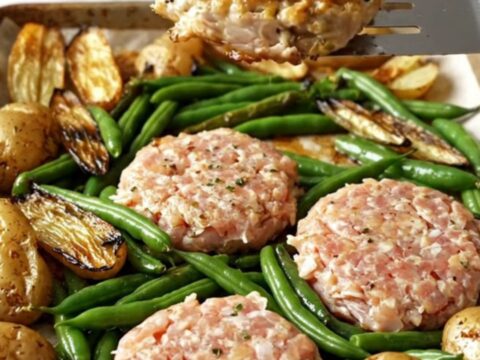 A sheet pan filled with golden-brown turkey patties, roasted baby potatoes, and blistered green beans.