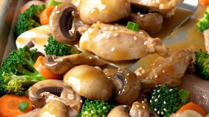 A sheet pan filled with golden roasted chicken breast chunks, mushrooms, broccoli, and carrots drizzled with a savory sauce.