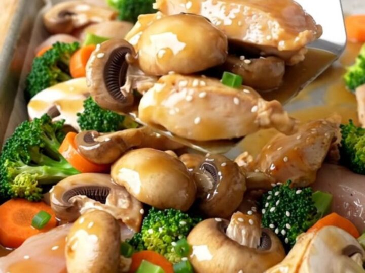 A sheet pan filled with golden roasted chicken breast chunks, mushrooms, broccoli, and carrots drizzled with a savory sauce.
