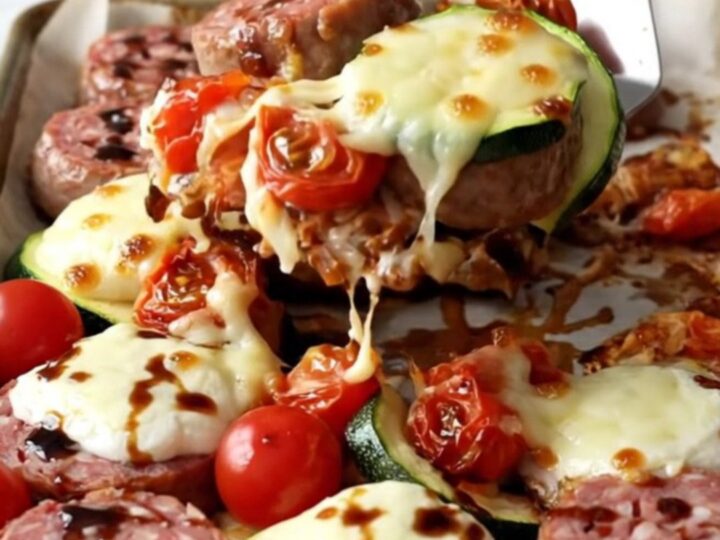 A rustic sheet pan filled with golden-brown Italian sausage, roasted zucchini, and blistered cherry tomatoes