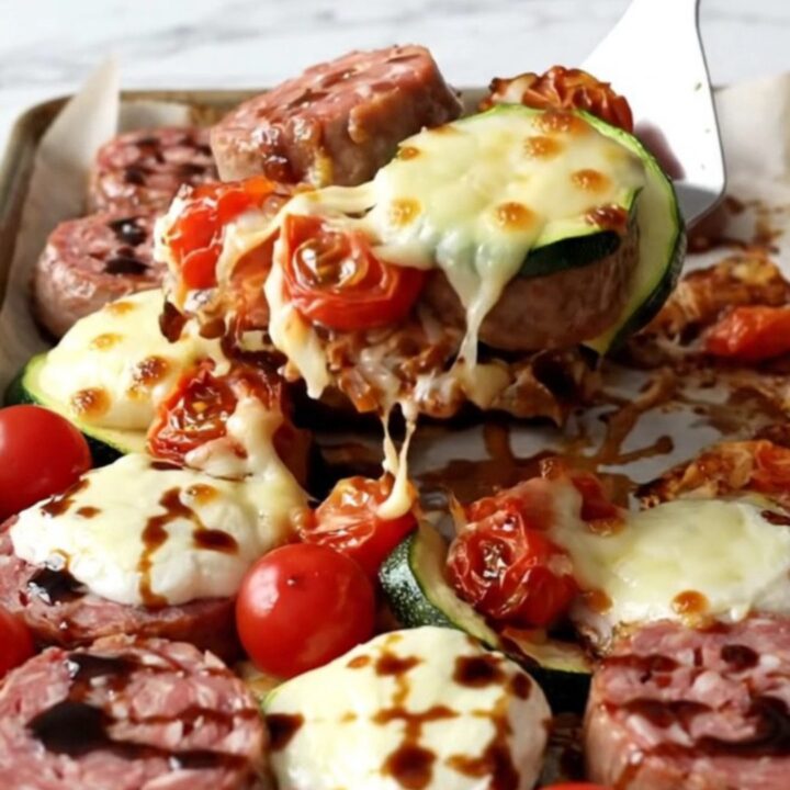 A rustic sheet pan filled with golden-brown Italian sausage, roasted zucchini, and blistered cherry tomatoes