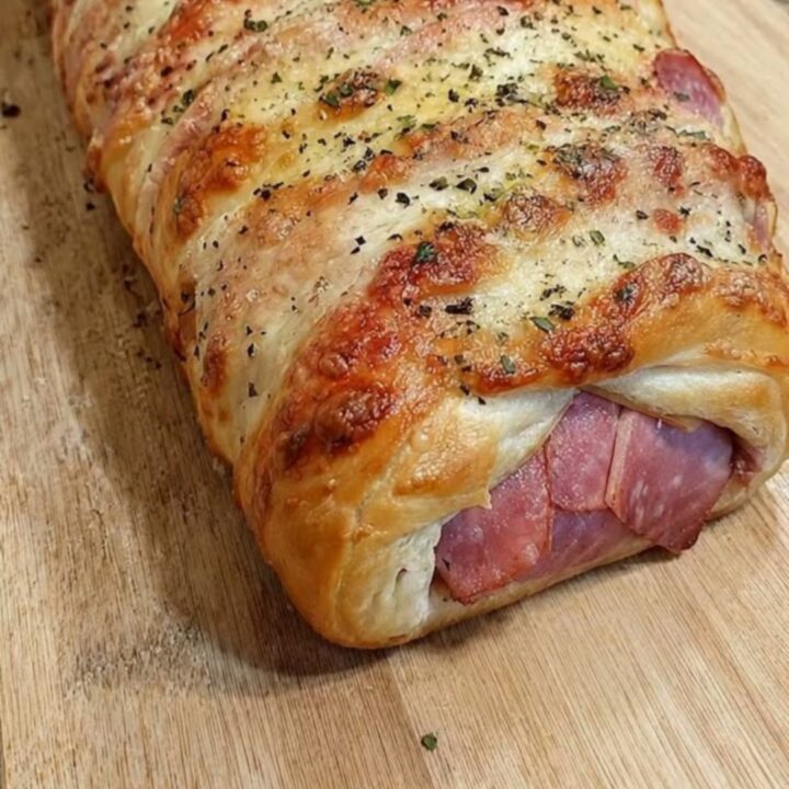 A golden-brown baked ham and cheese stromboli resting on a wooden cutting board with a slice showing melted cheese.