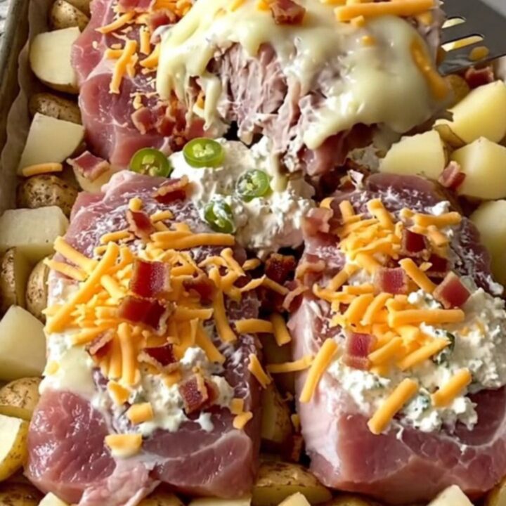 A sheet pan filled with golden roasted potatoes and pork chops topped with melted jalapeno cream cheese, cheddar