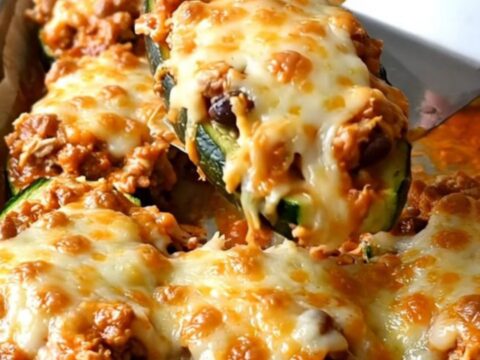 A row of freshly baked enchilada zucchini boats topped with melted cheese and fresh cilantro on a parchment-lined sheet pan.
