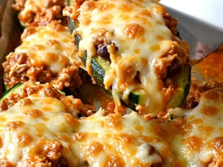 A row of freshly baked enchilada zucchini boats topped with melted cheese and fresh cilantro on a parchment-lined sheet pan.