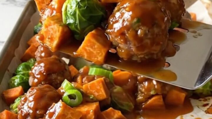 A sheet pan filled with golden turkey meatballs, roasted sweet potatoes, and Brussels sprouts drizzled in a rich red sauce.