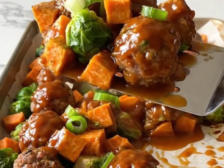 A sheet pan filled with golden turkey meatballs, roasted sweet potatoes, and Brussels sprouts drizzled in a rich red sauce.