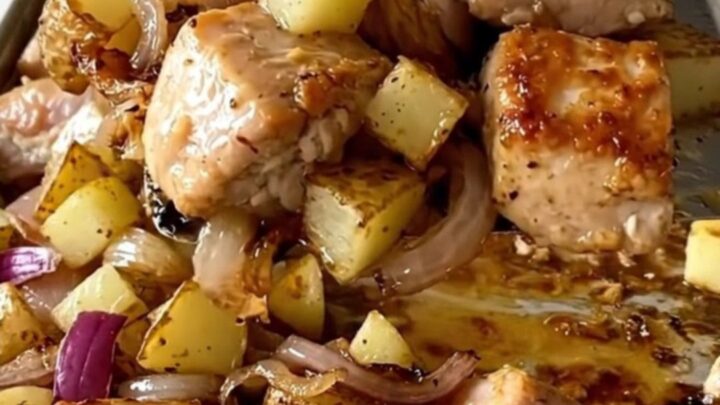 A sheet pan filled with golden roasted chicken chunks, crispy diced potatoes, and soft, caramelized red onions.