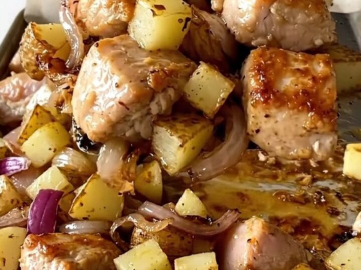 A sheet pan filled with golden roasted chicken chunks, crispy diced potatoes, and soft, caramelized red onions.