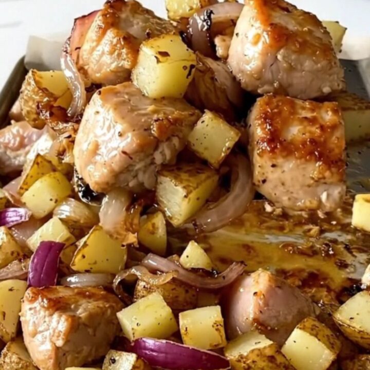 A sheet pan filled with golden roasted chicken chunks, crispy diced potatoes, and soft, caramelized red onions.